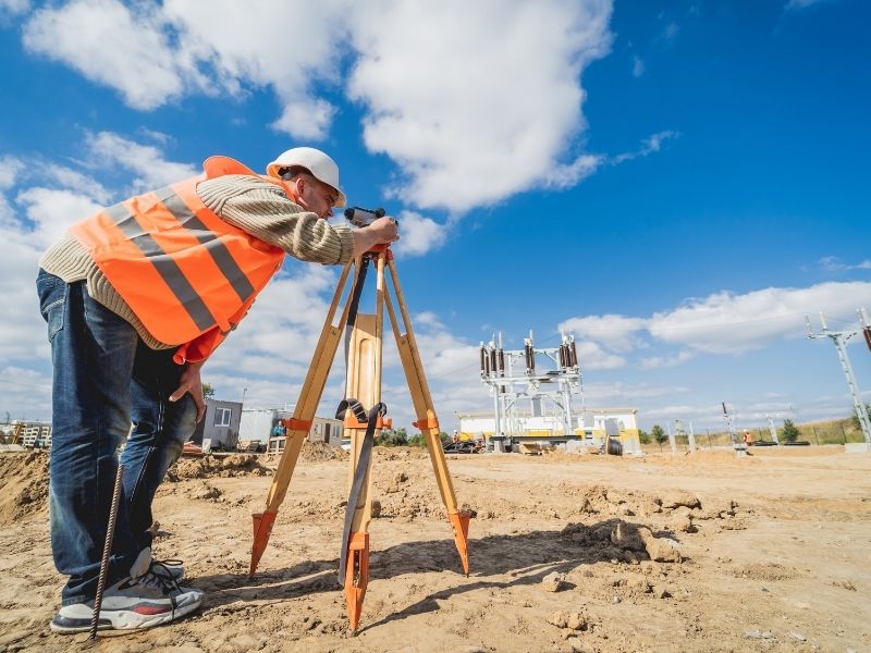 Licensed surveyor performing field measurements with surveying equipment at an active property development site